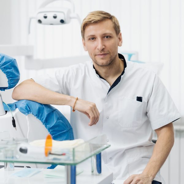 Portrait of a positive young male dentist in uniform at the dental office